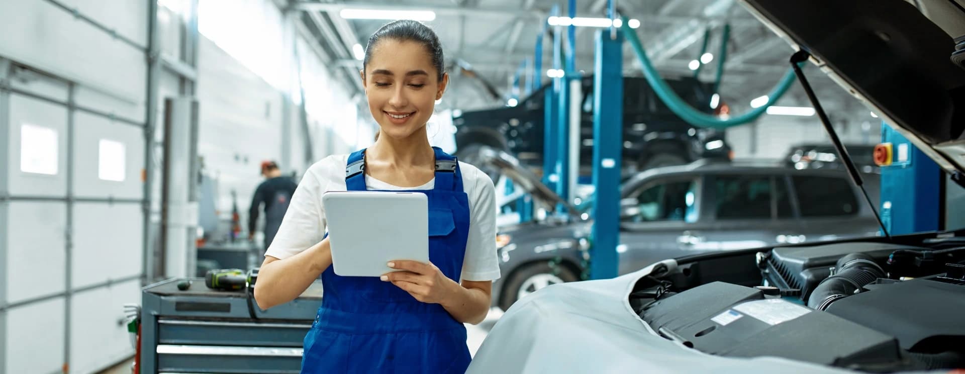 A technician checking a tablet beside a car with its bonnet open